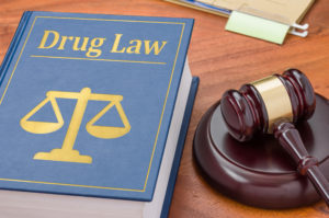 book with "drug law" and golden justice scales on the cover alongside a gavel on a wooden surface