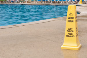 yellow caution sign warning of a slippery surface next to a swimming pool p