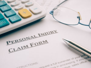 personal injury claim form surrounded by a calculator, glasses, and a pen that a personal injury attorney might use