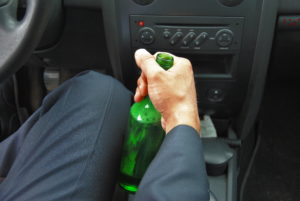 driver holding a green bottle of alcoholic beverage while in the driver seat of a car