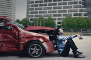 man sitting in front of his wrecked car