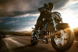 man in motorcycle speeding through a country road at sunset