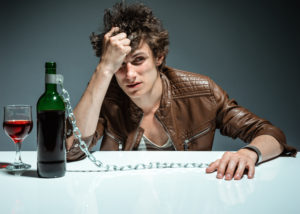 disappointed young man handcuffed to a bottle of alcoholic drink