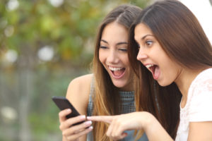 two girls looking at a cell phone with shocked and joyful expressions on their faces