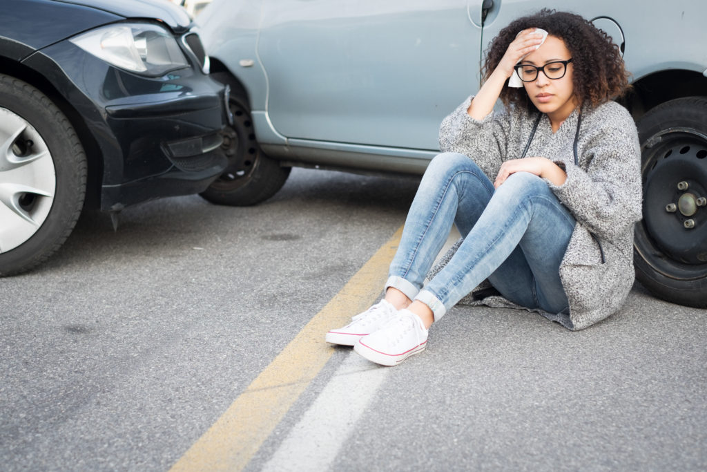 Young woman sitting by her car on the ground after a car accident